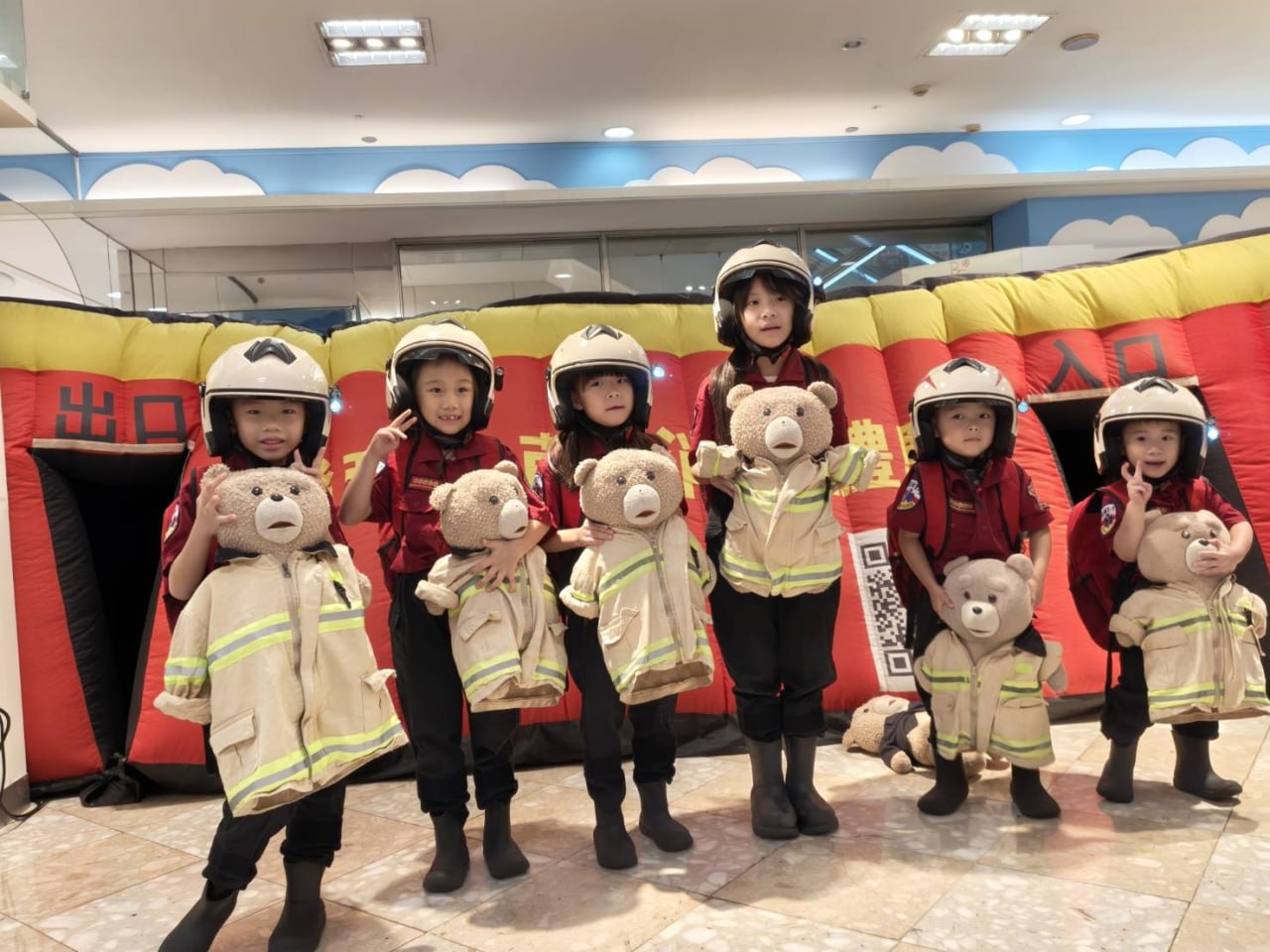 孩子們穿著消防衣與頭盔,抱著小熊在消防體驗帳前合照